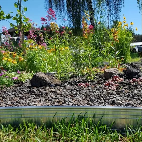 Metall Rasenkante aus verzinktem Stahl zur Einfassung eines Blumenbeets mit Schotter und verschiedenen Stauden in einem Garten.