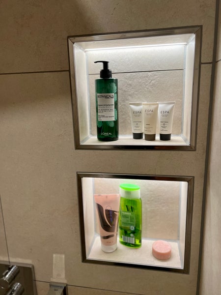 Zwei beleuchtete Wandnischen im Badezimmer mit verschiedenen Pflegeprodukten wie Shampoo und Duschgel auf Ablageflächen aus Fliesen.