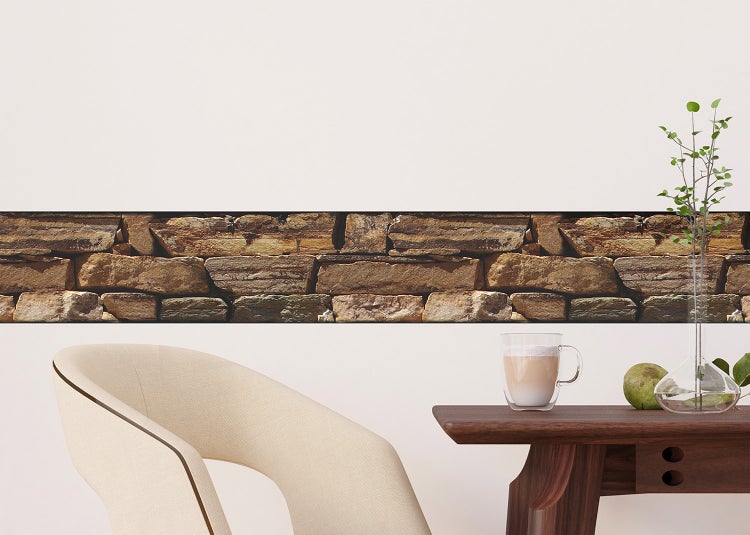 Selbstklebende Tapetenbordüre in Natursteinoptik an einer hellen Wand in einem modern eingerichteten Raum mit Stuhl und Holztisch.