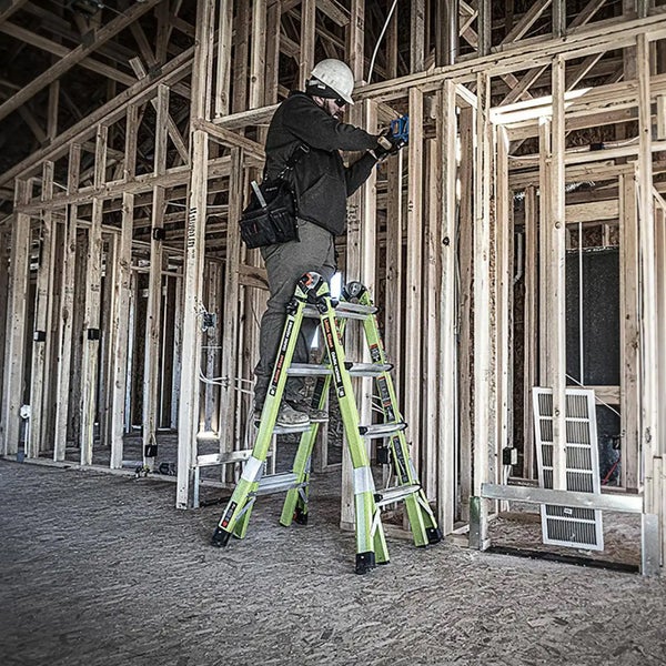 Handwerker auf einer grünen Mehrzweckleiter bei Montagearbeiten im hölzernen Rohbau eines Hauses.