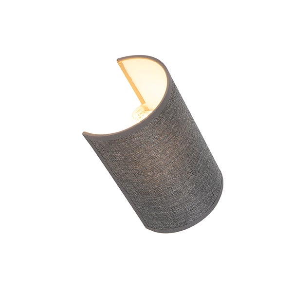 Moderne Wandleuchte mit gebogenem Textilschirm und eingeschaltetem Leuchtmittel.