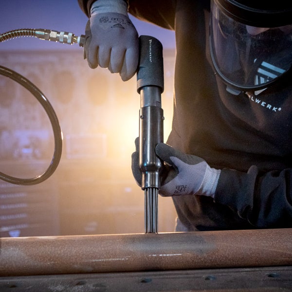 Eine Person bedient einen Nadelentroster von Stahlwerk, um eine Metalloberfläche zu reinigen.