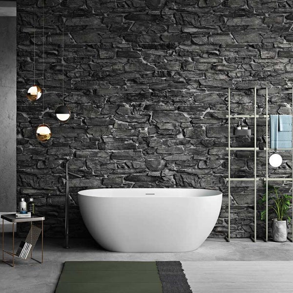 Freistehende Badewanne vor einer Wand in Natursteinoptik in einem modernen Badezimmer mit Accessoires und Beleuchtung.