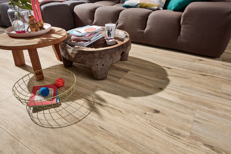 Wohnzimmer mit hellem Laminatboden in Holzoptik, kombiniert mit einem rustikalen Holztisch und einem bequemen Sofa im Hintergrund.