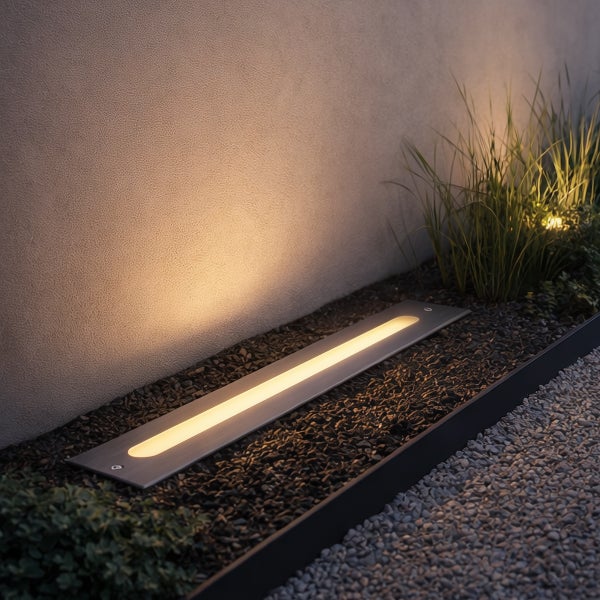 Rechteckige LED-Bodeneinbauleuchte für den Außenbereich, in Kies installiert, beleuchtet eine verputzte Wand.