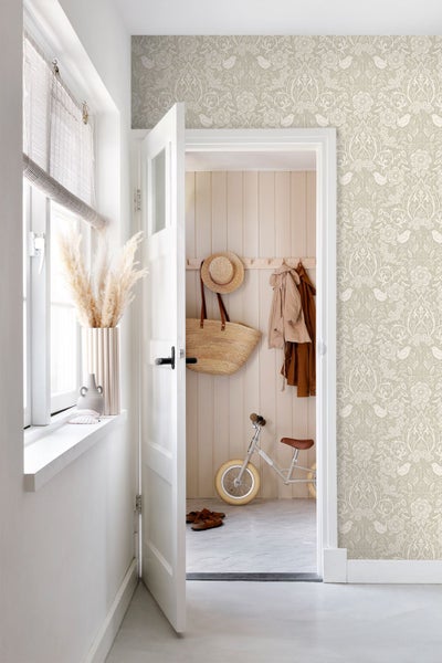 Helle Diele mit Vliestapete mit Blumen- und Vogelmuster, offener weißer Tür und Blick auf eine Garderobe mit Laufrad und Strohtasche.