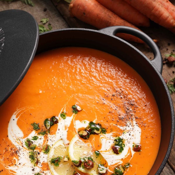 Karottensuppe in einem Kochtopf mit Deckel, garniert mit Zitrone und Kräutern.