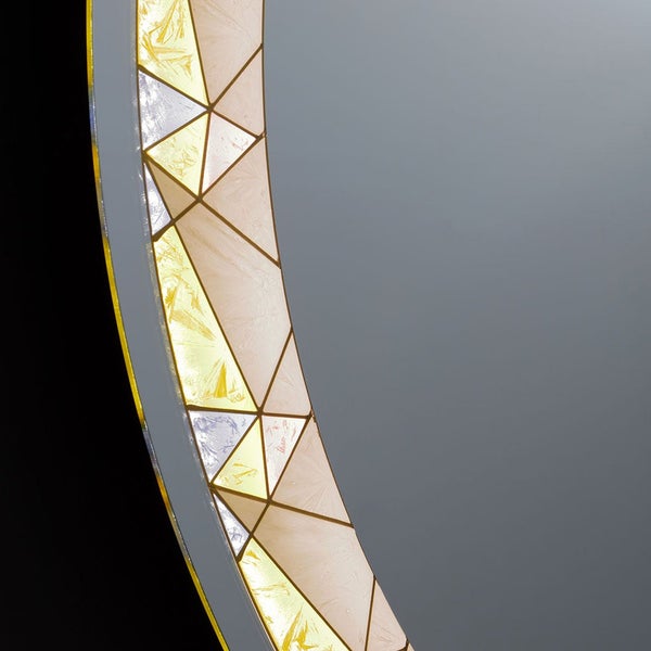 Detailansicht runder Badspiegel mit beleuchtetem Rand in geometrischem Dreiecksmuster und Kristallglasoptik.