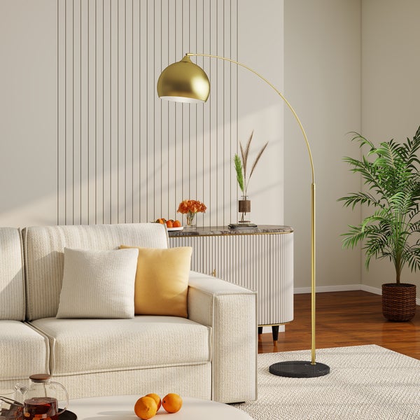 Goldene Bogenlampe mit Marmorfuß in einem modernen Wohnzimmer neben einem Sofa mit Kissen und einer Zimmerpflanze.
