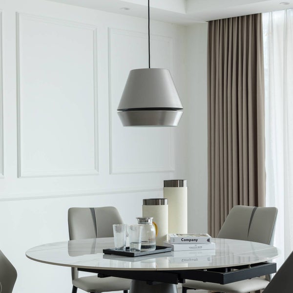 Moderne Pendelleuchte mit Metallschirm über rundem Marmortisch in hellem, geordnetem Esszimmer mit grauen Stühlen und Wandpaneelen.