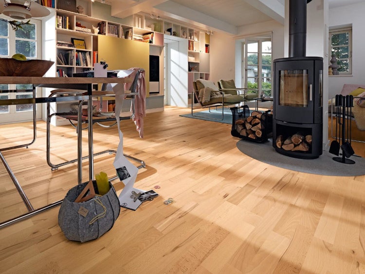 Parkettboden in hellem Holzdesign in einem modern eingerichteten Wohnzimmer mit Kaminofen, Esstisch und Bücherregal.