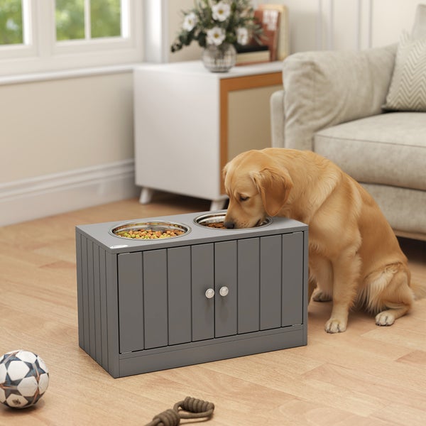 Golden Retriever frisst an einer grauen, erhöhten Futterstation aus Holz mit zwei Edelstahlschüsseln in einem hellen Wohnzimmer.