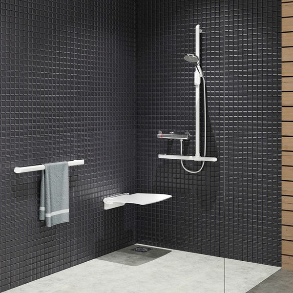 Barrierefreie Dusche mit schwarzen Mosaikfliesen, weißem Duschklappsitz, Haltegriffen und einer modernen Duscharmatur.