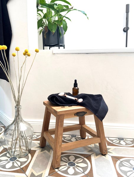 Badezimmer Stillleben mit Holzschemel, Handtuch, Hautpflegeprodukten und Blumenarrangement