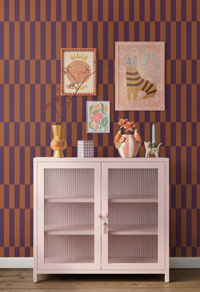 Vliestapete mit violett-braunem Karomuster hinter einer rosa Vitrine mit geriffelten Glastüren und bunter Dekoration.