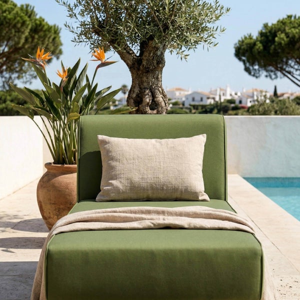Modernes grünes Gartensofa mit beigem Kissen und Decke an einem Pool mit Olivenbaum und Strelitzie im Tontopf.