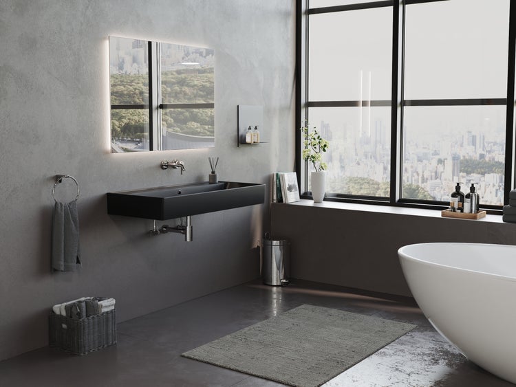 Badezimmer mit schwarzem Waschtisch, beleuchtetem Spiegel und freistehender Badewanne vor einem Fenster