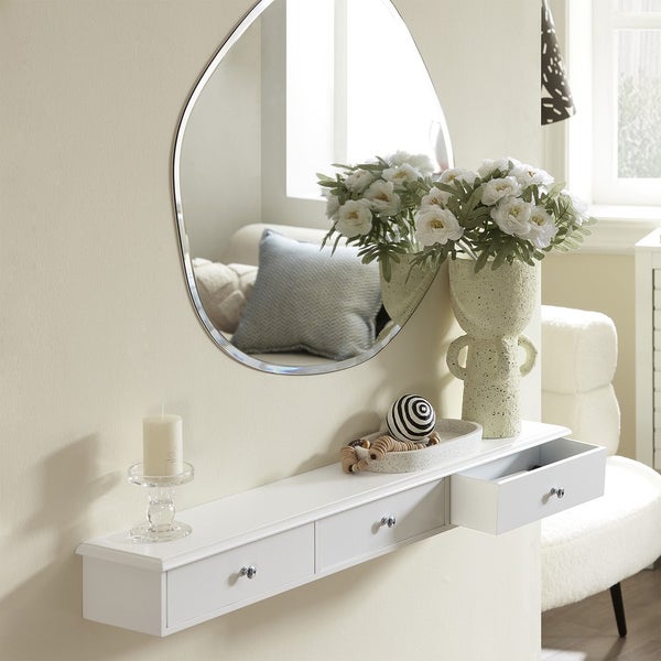 Wandspiegel über einer weißen Konsole mit Schubladen, dekoriert mit Blumen und Kerze.