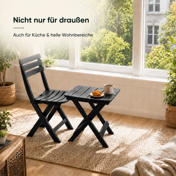 Ein klappbarer Stuhl und ein klappbarer Tisch aus Holz in einem hellen Wohnbereich mit großen Fenstern und Zimmerpflanzen.