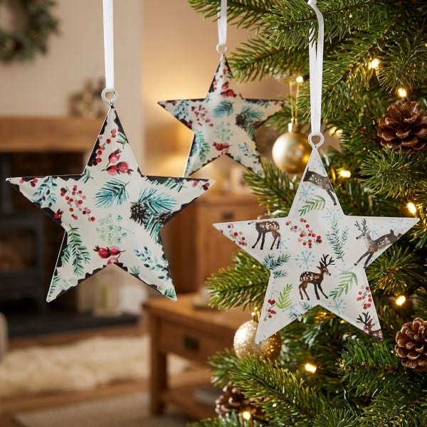 Drei hängende Weihnachtssterne aus Metall mit weihnachtlichem Dekor aus Tannenzweigen, Beeren und Rehen als Baumschmuck am Weihnachtsbaum.