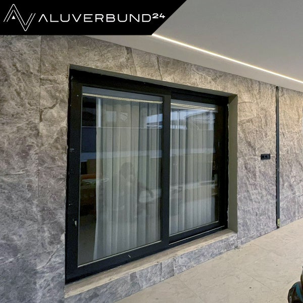 Aluverbund24 Logo neben einem Schiebefenster in einer Steinmauer.