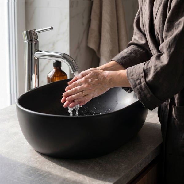 Eine Person wäscht sich die Hände über einem schwarzen Aufsatzwaschbecken mit einer chromglänzenden Armatur in einem modernen Badezimmer.
