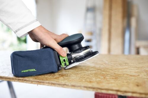 Ein Mann benutzt einen Exzenterschleifer der Marke Festool, um ein Holzbrett zu schleifen.