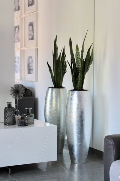 Große silberne Bodenvase mit Bogenhanf in modernem Wohnraum neben weißem Sideboard mit Dekoration.