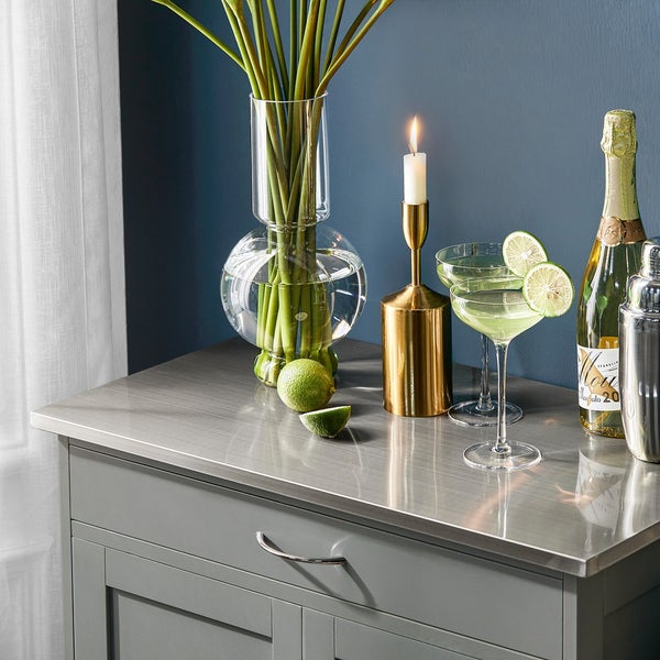 Dekoratives Stillleben mit Blumenvase, Kerzenständer, Getränken und Limetten auf einer Kommode