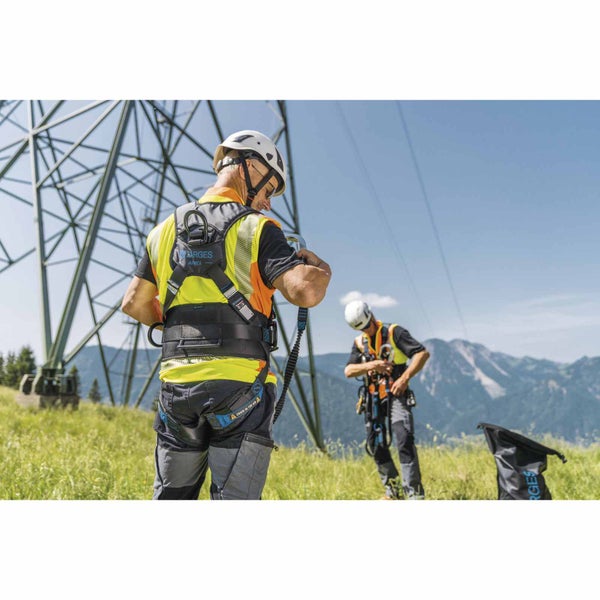 Handwerker mit Auffanggurt mit Zarges Logo und Helm bei Arbeiten an einem Strommast in einer hellen bergigen Umgebung.