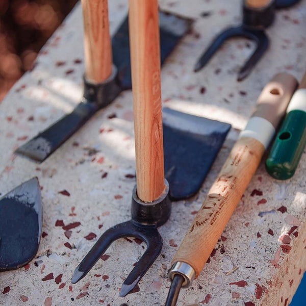 Verschiedene Gartenhandwerkzeuge aus Metall mit Holzstielen auf einer gemusterten Unterlage.