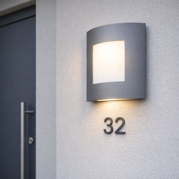 Moderne Außenwandleuchte in Anthrazit mit Lichtaustritt nach vorne und unten, montiert an einer hellen Hauswand über der Hausnummer 32.