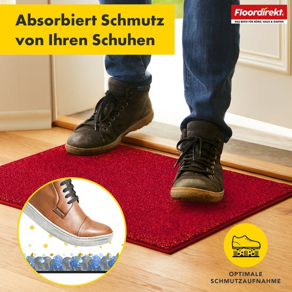 Roter Fußabtreter vor einer Tür mit Schuhen darauf, der Schmutz absorbiert