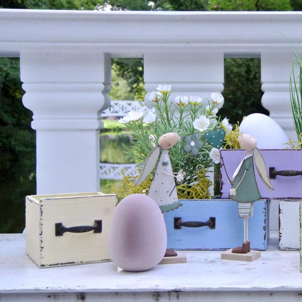 Dekorative Szene mit Holzhasen, Osterei und Blumenkästen auf einer Terrasse