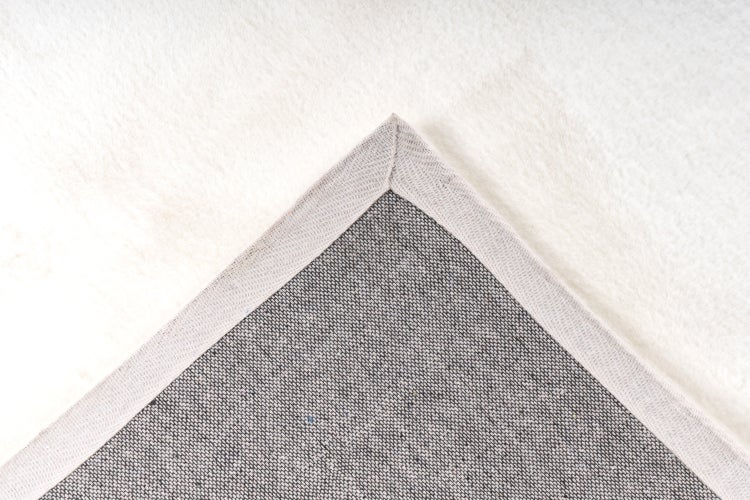 Detailansicht einer Teppichrückseite mit Textilrücken und gekettelter Kante auf einem weichen Florbelag.