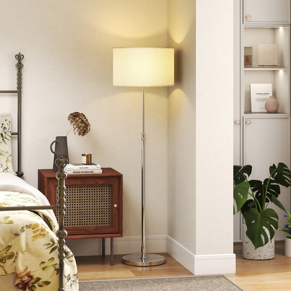 Moderne Stehleuchte mit zylindrischem Lampenschirm neben einem Nachttisch mit Rattangeflecht in einem gemütlichen Schlafzimmer.
