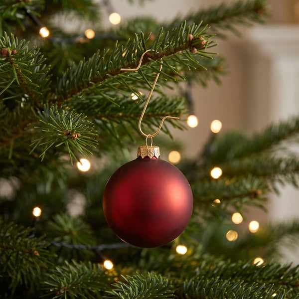 Weihnachtskugel mit Aufhänger an einem Tannenbaum mit Lichterkette.