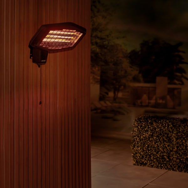 Vonroc Infrarot Wandheizstrahler an einer Holzwand im Außenbereich montiert, strahlt warmes Licht auf eine Terrasse bei Nacht.