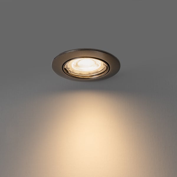 Runder LED-Einbaustrahler aus Metall in Edelstahloptik, eingeschaltet mit warmweißem Lichtstrahl an einer Wand.