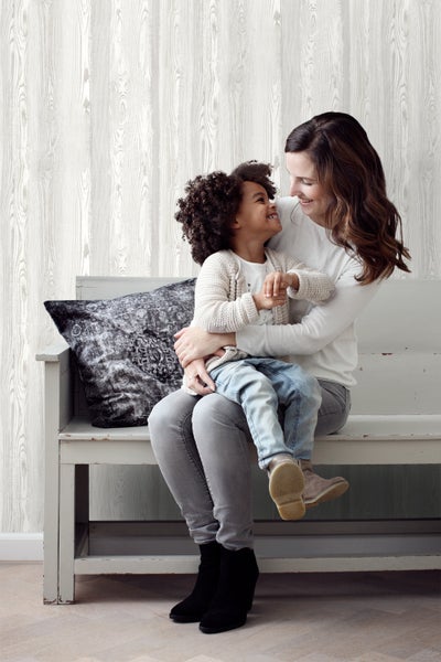 Mutter und Kind sitzen vor einer Wandtapete mit Holzoptik auf einer Bank