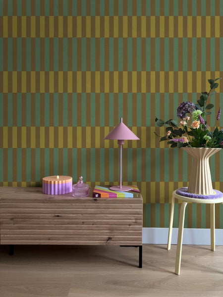 Modernes Interieur mit geometrisch gemusterter Tapete, einem Sideboard aus Holz, einer Tischlampe und einer Blumenvase auf einem Hocker.