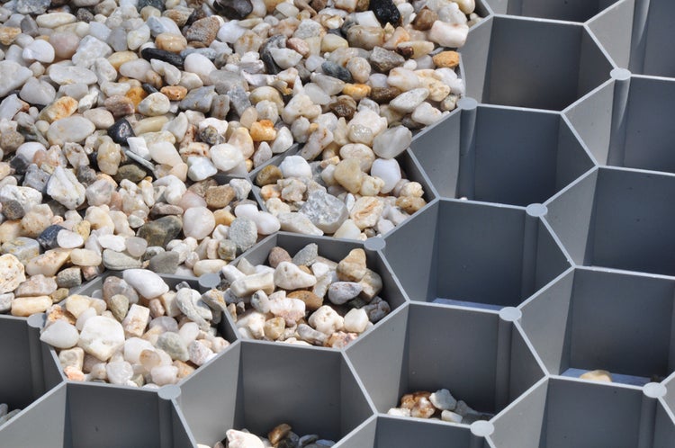 Kiesstabilisierungsgitter aus grauem Kunststoff mit Wabenstruktur, teilweise befüllt mit hellem Kies.