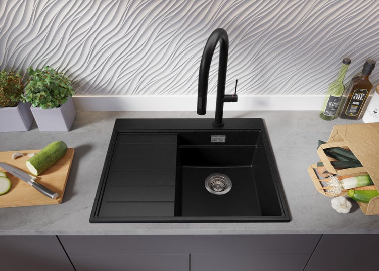 Schwarzes Spülbecken mit Abtropffläche und schwarzer Armatur auf einer Küchentheke mit Gemüse und Kräutern.