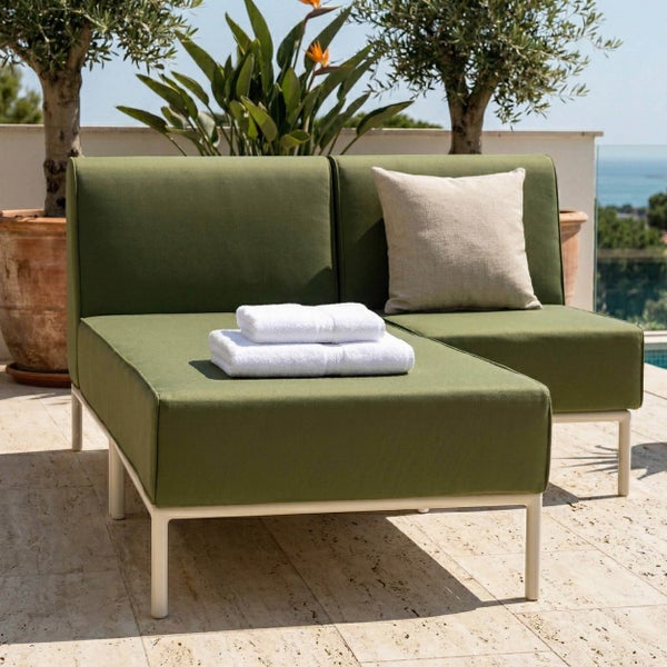 Modernes Garten-Lounge-Set mit grünen Polstern und weißem Metallgestell auf einer sonnigen Terrasse mit Olivenbäumen und Meerblick.