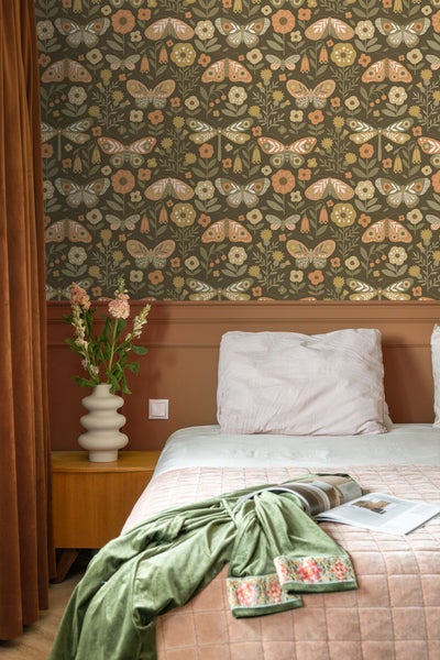 Schlafzimmer mit gemusterter Tapete, Bett, Nachttisch und Blumenvase.