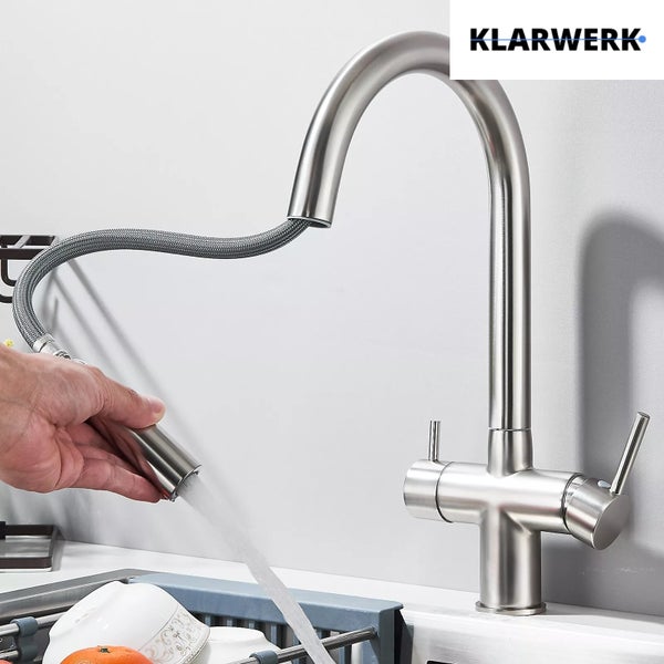 Küchenarmatur aus Edelstahl mit herausziehbarer Geschirrbrause in Benutzung über einer Spüle. KLARWERK Logo.
