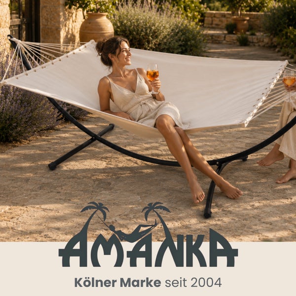 Eine Frau entspannt in einer großen Hängematte mit Metallgestell auf einer Steinterrasse in einem hellen Garten. Amanka Logo.