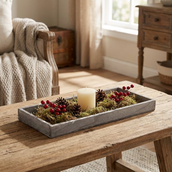 Dekoratives Holztablett mit Kerze, Tannenzapfen und Beeren, als Tischdeko auf einem rustikalen Holztisch in einem Wohnzimmer.