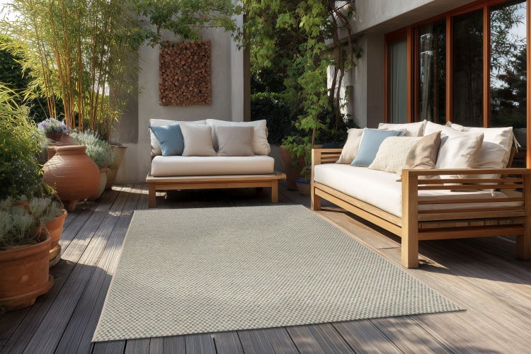 Outdoor Teppich mit geometrischem Muster auf einer Holzterrasse mit Lounge Möbeln in einem sonnigen Gartenbereich.