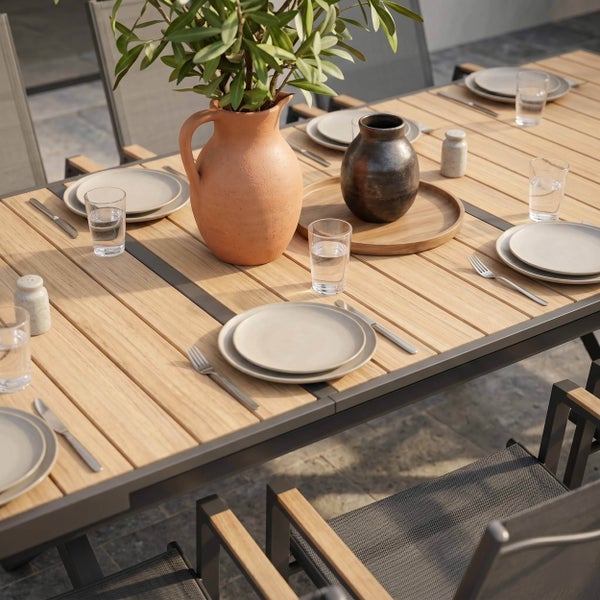 Moderner Gartenstuhl mit Metallgestell, Textilbespannung und Holzarmlehnen an einem Esstisch auf einer hellen gepflasterten Terrasse.